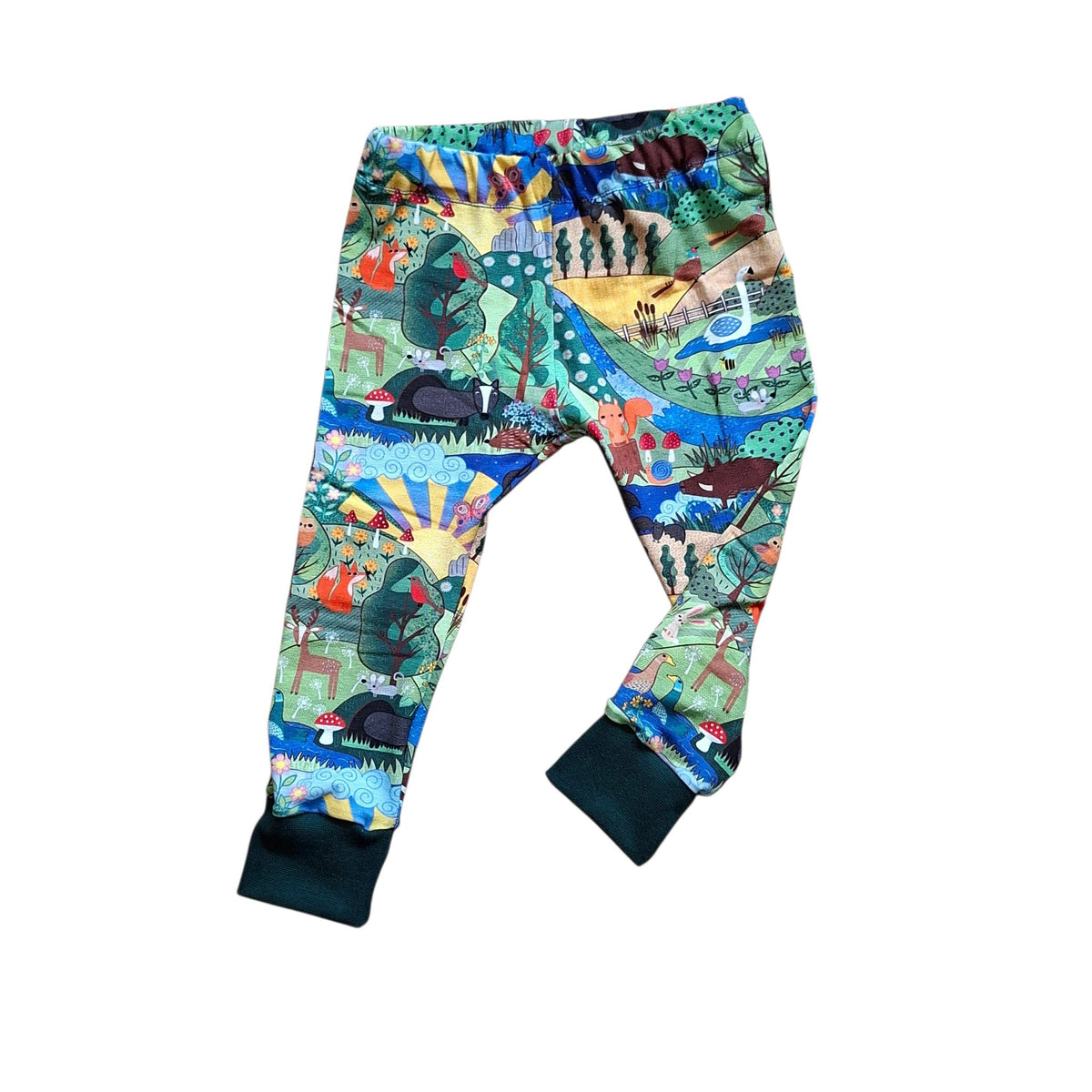 A pair of children's leggings featuring a vibrant, multicolor nature-themed print with illustrations of trees, animals, and landscapes. The pants have solid dark teal ribbed cuffs at the ankles and an elastic waistband, shown against a plain white background.