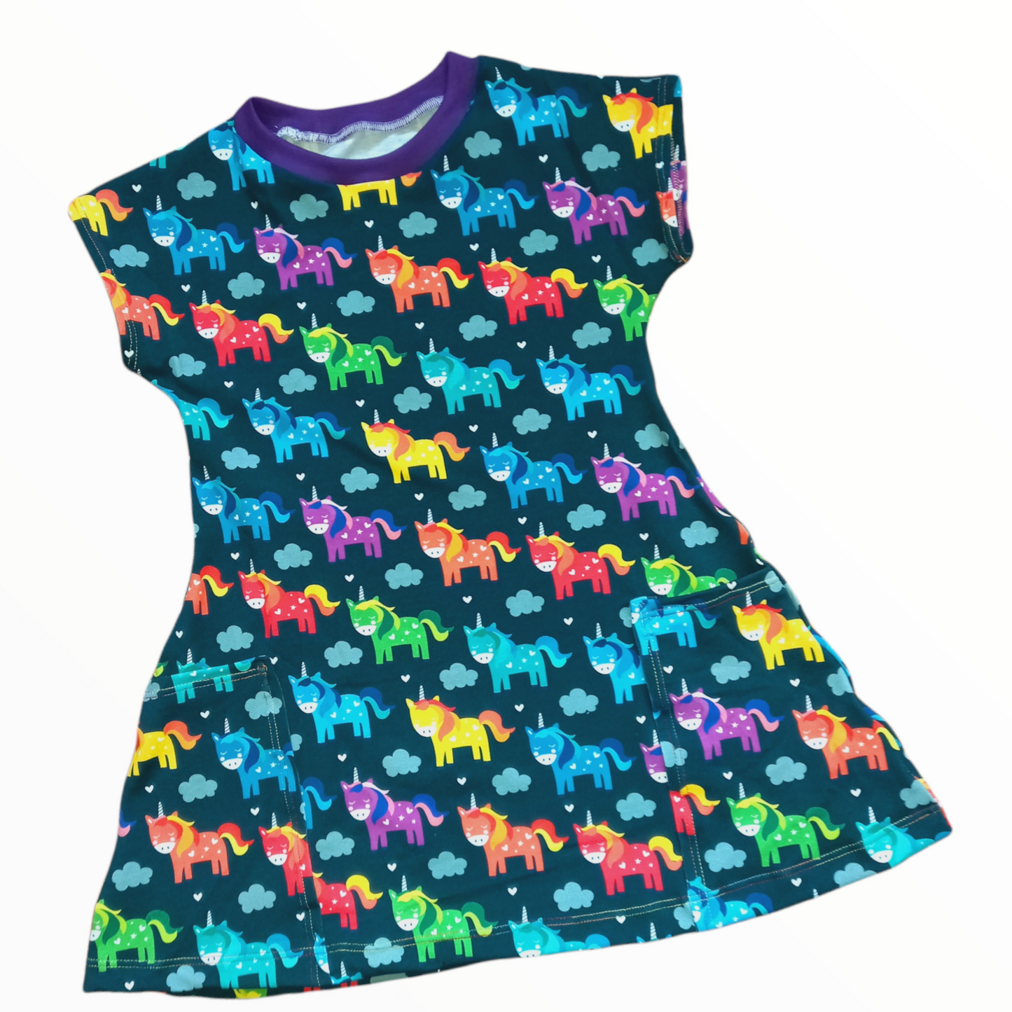 Navy blue fabric with rainbow coloured unicorns on a childrens dress with pockets on the front