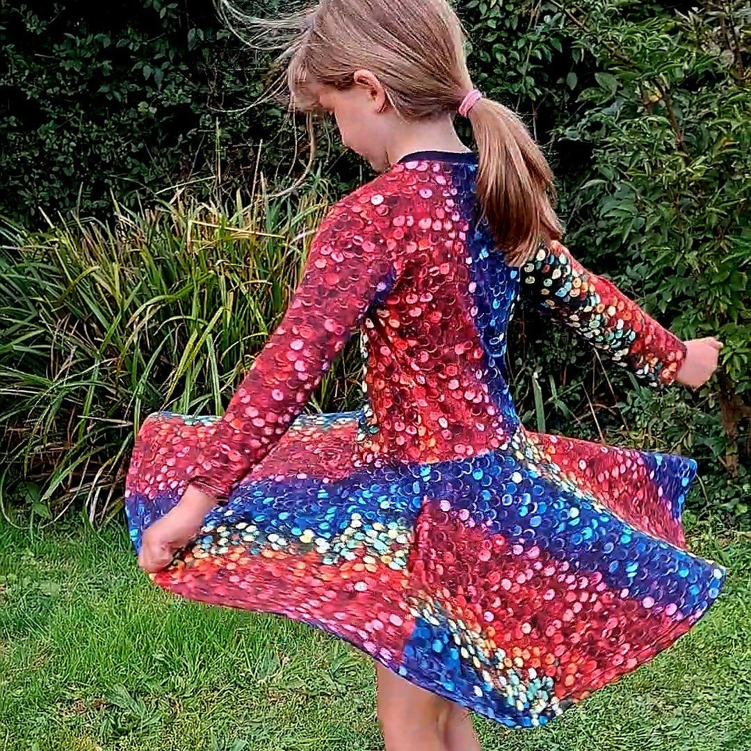 Child twirling outdoors in a long-sleeved rainbow sequin-print Twirly Swirly dress