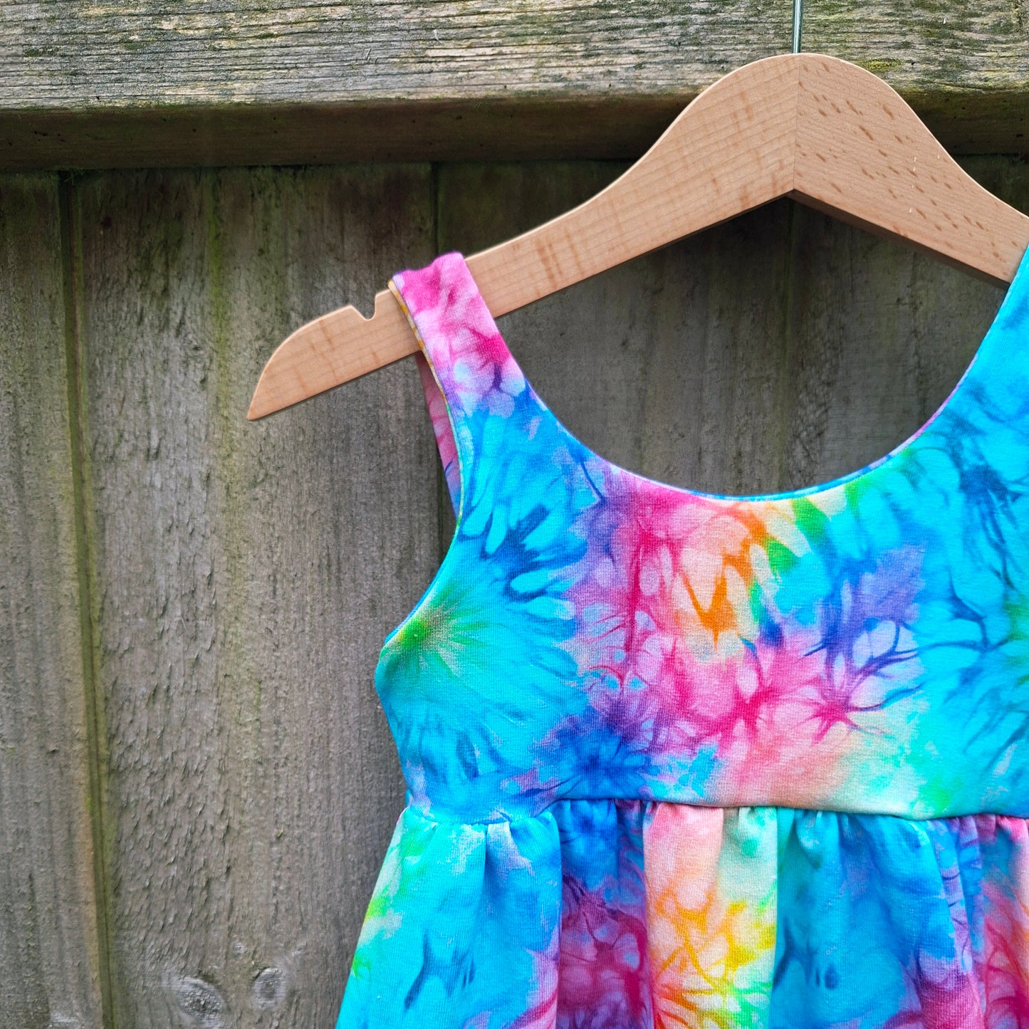 Colourful tie-dye romper on a wooden hanger against a wooden background