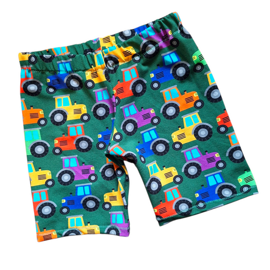 Children's knee length shorts in a green fabric with rainbow coloured tractors
