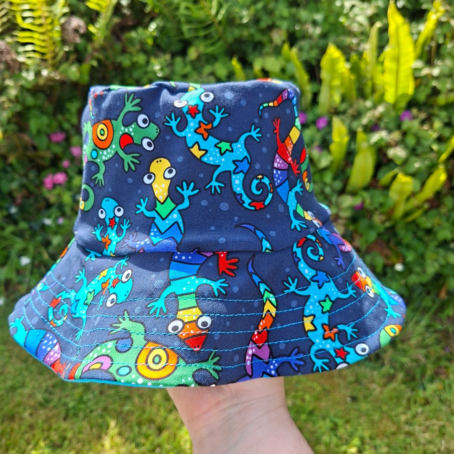 Children's bucket hat with colorful lizard pattern held by a person outdoors.
