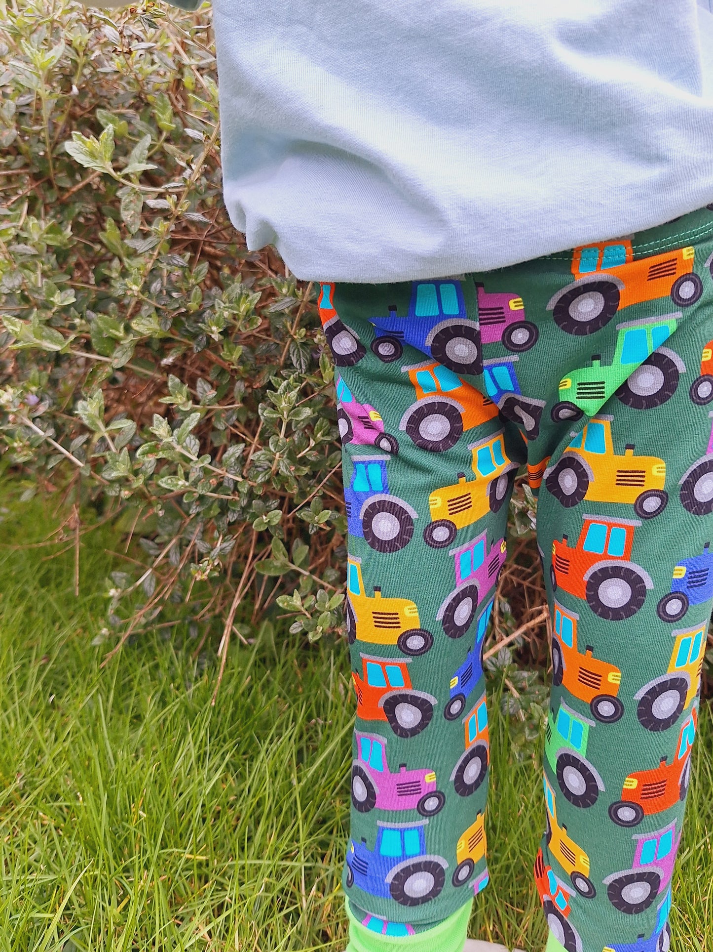 Tractor print childrens leggings made in the UK. On a dark green background rainbow coloured tractors are the perfect farm print