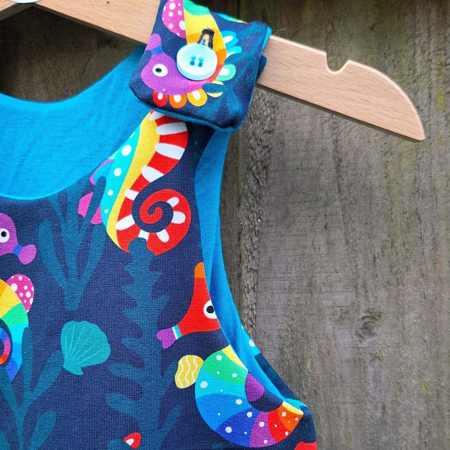 Colourful children's dunagrees with seahorse design on a wooden hanger against a wooden background