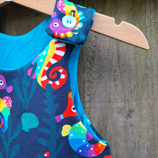 Colourful children's dunagrees with seahorse design on a wooden hanger against a wooden background