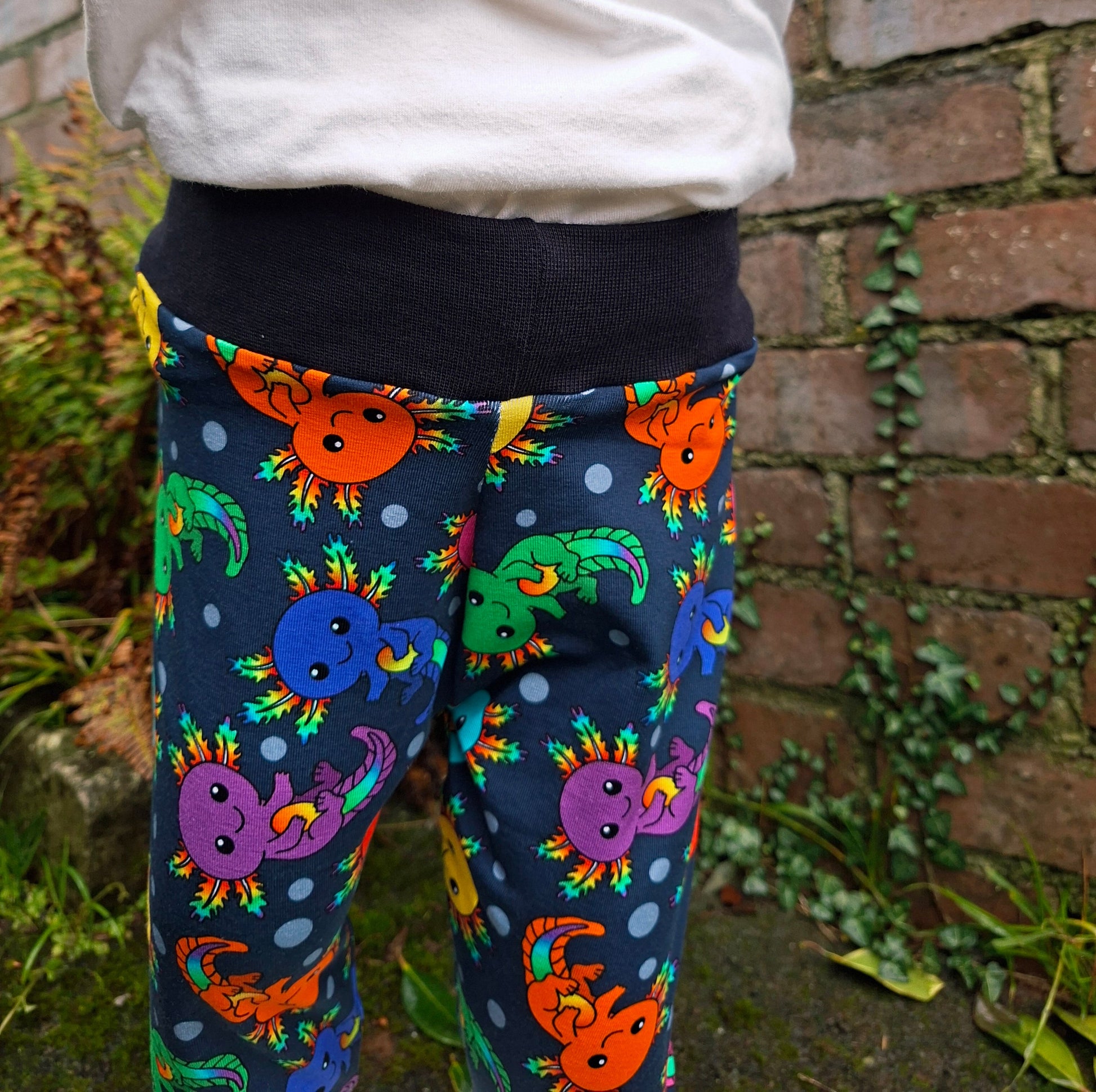 Colourful axolotl trousers worn by a person sitting on a stone wall.