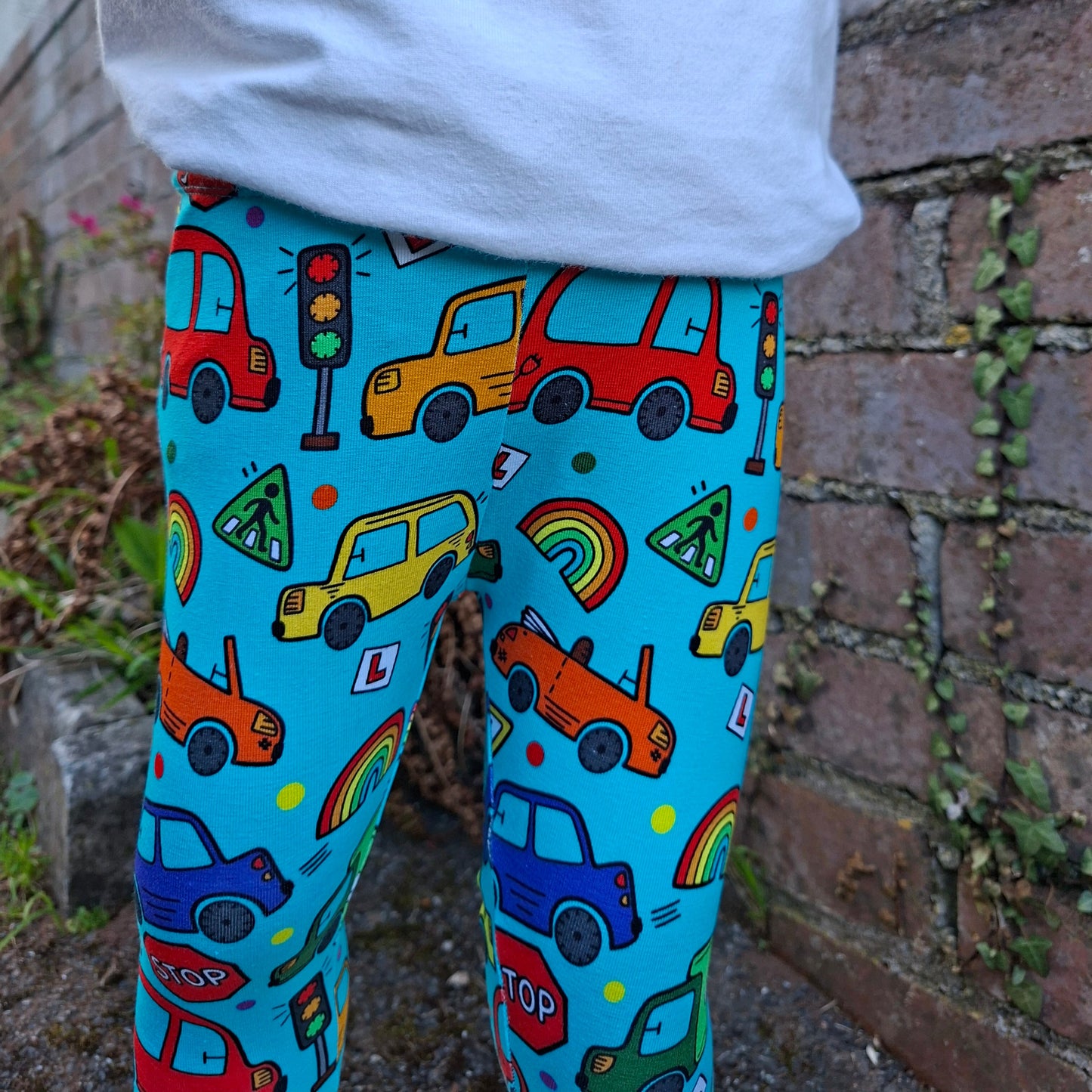 Colorful patterned leggings with cars and rainbows worn by a person, standing on a stone surface.