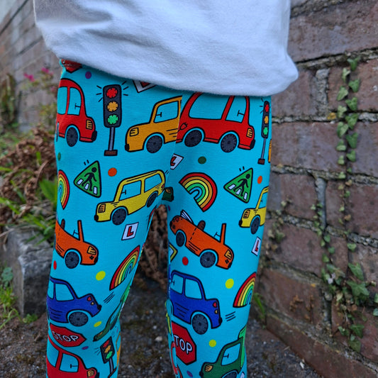 Colorful patterned leggings with cars and rainbows worn by a person, standing on a stone surface.