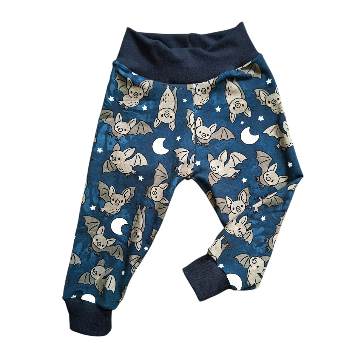 A pair of children's relaxed fit trousers featuring a dark blue night-sky pattern with cartoon bats, crescent moons, and stars, finished with solid navy cuffs and waistband.