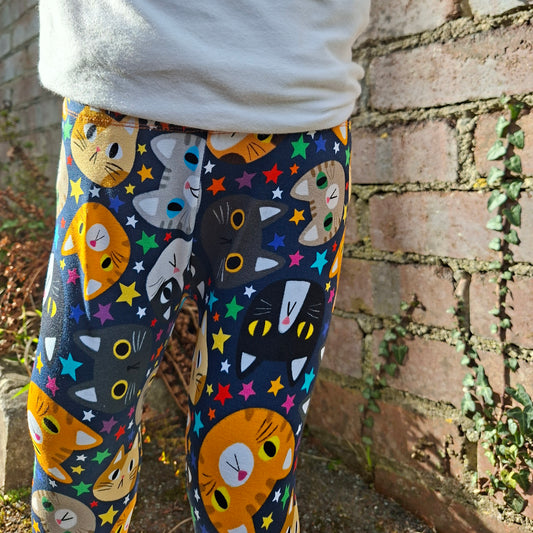 Colorful cat-patterned leggings worn by a person against a brick wall.