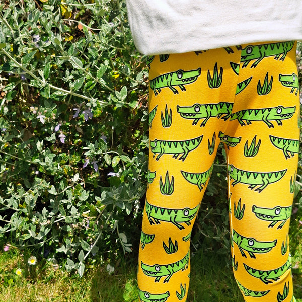 Yellow leggings with green crocodile pattern worn by a person on a grassy background