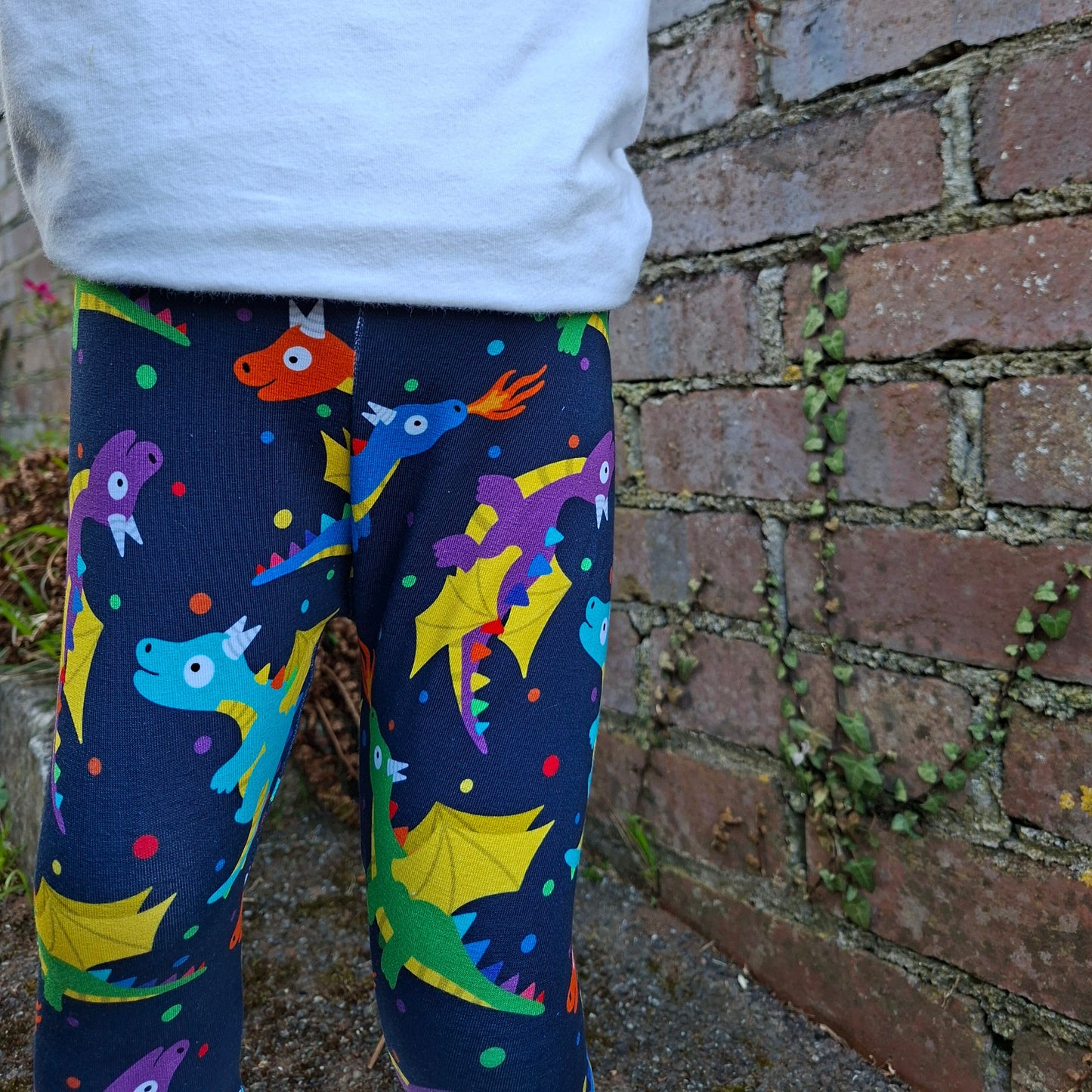 Colourful dragon leggings worn by a person on a brick pavement.