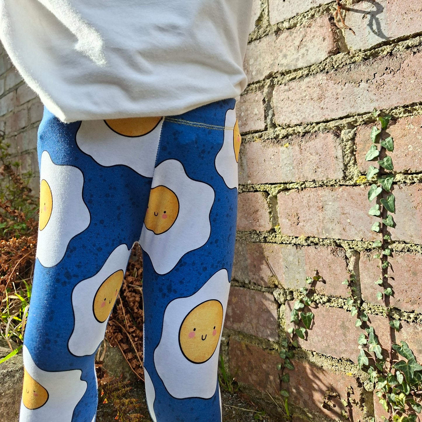 Person wearing leggings with egg pattern against a brick wall.