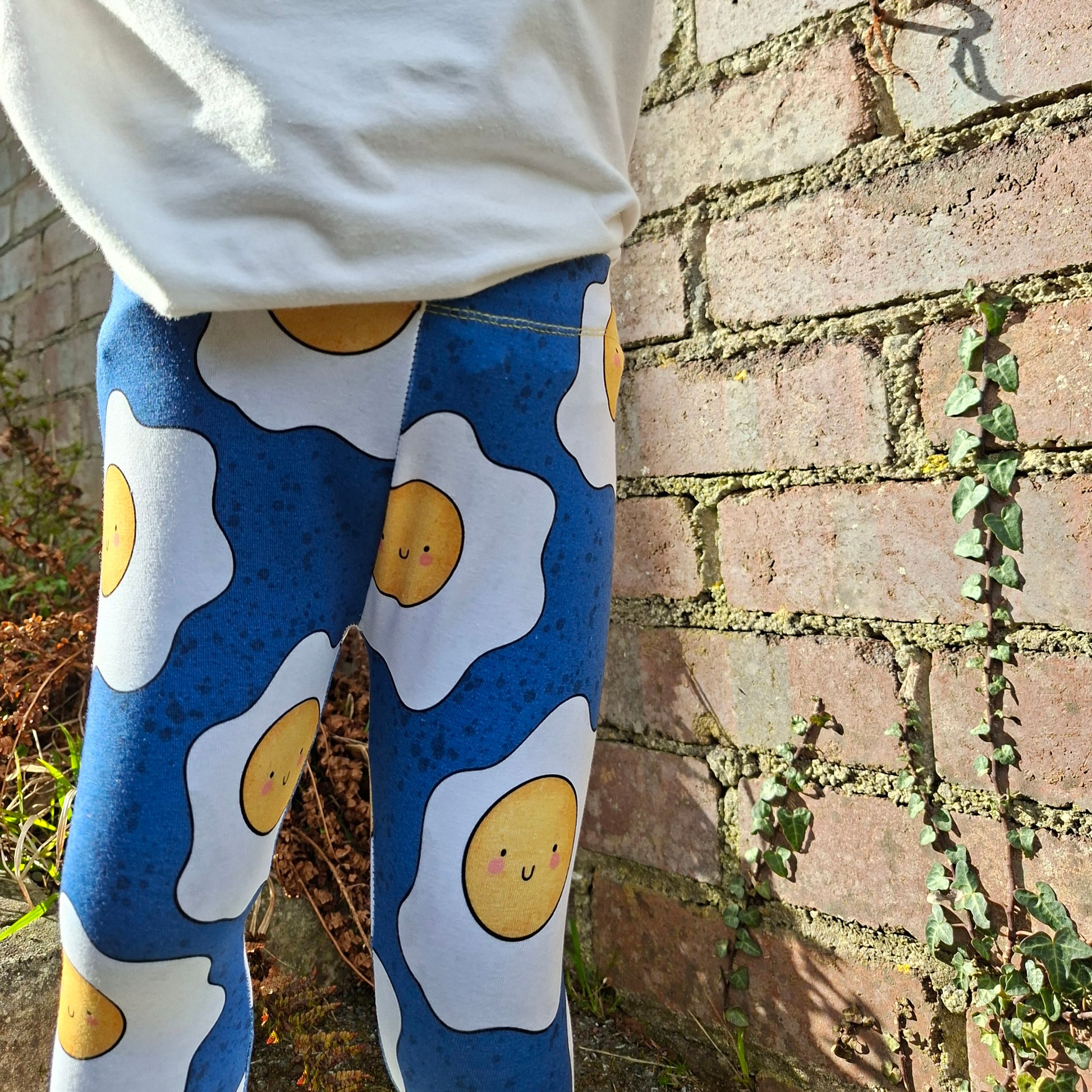 Person wearing leggings with egg pattern against a brick wall.