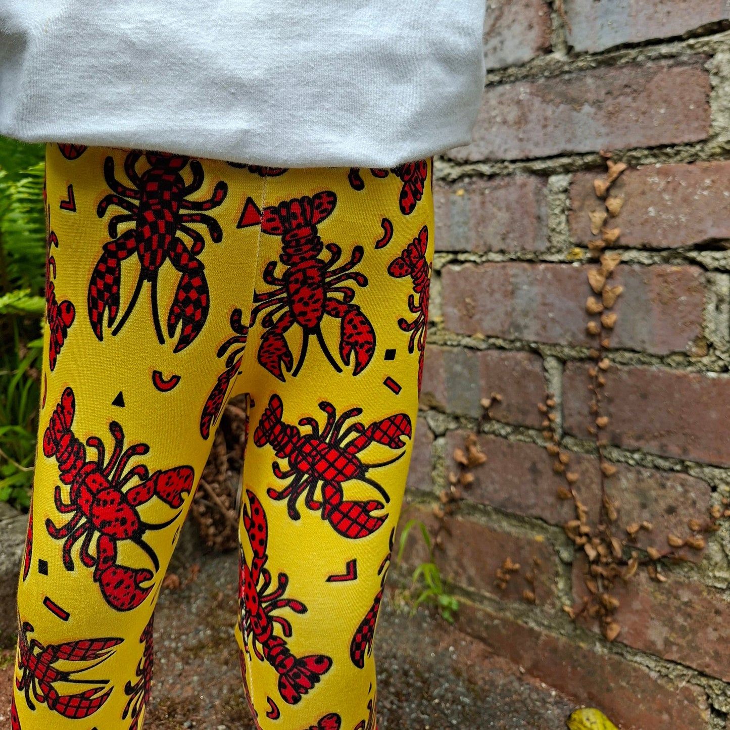 Yellow leggings with red lobster pattern worn by a child, against a brick wall background.