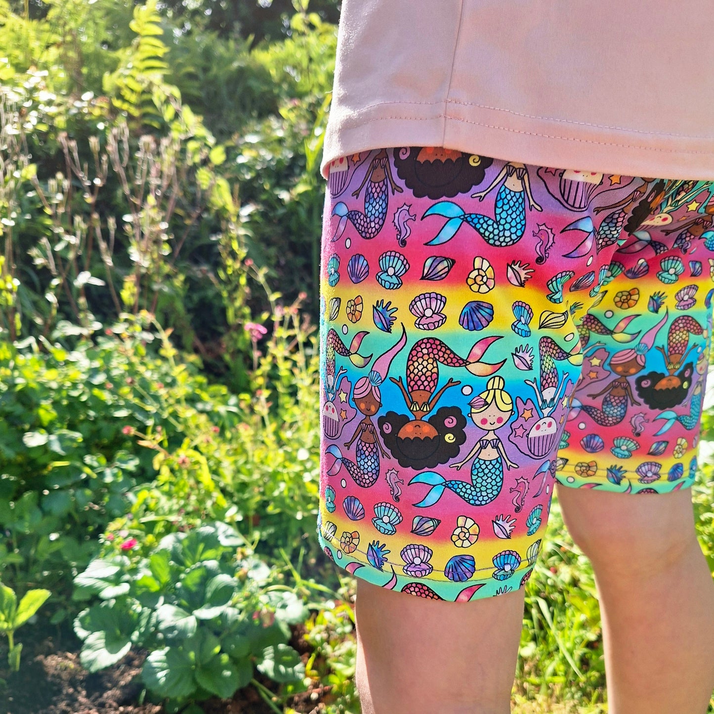 Colourful mermaid-patterned shorts worn by a child in a garden setting