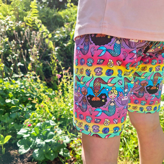 Colourful mermaid-patterned shorts worn by a child in a garden setting