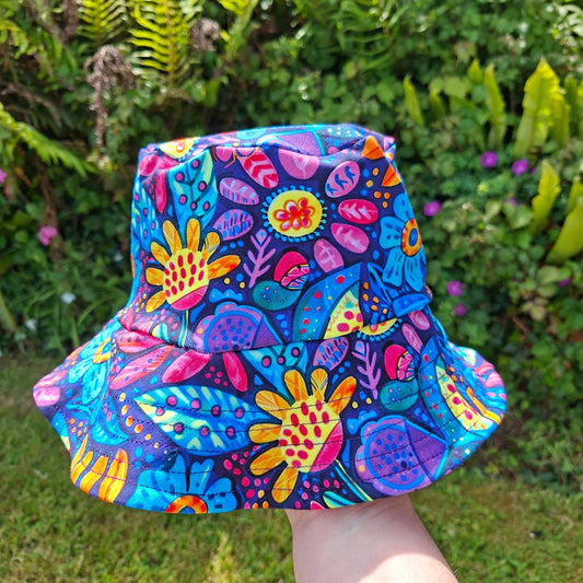 Colorful floral children's hat in a bucket style held by a person against a green outdoor background
