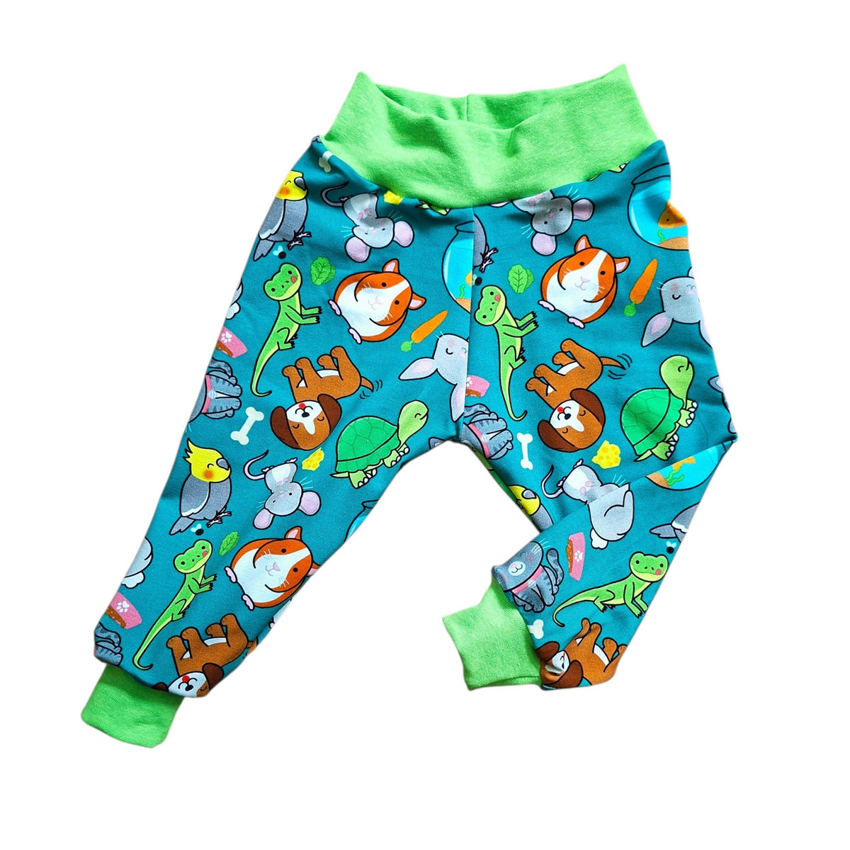 A pair of toddler relaxed fit trousers with a bright teal blue background covered in a colorful cartoon animal print, featuring lime green elastic waistband and cuffs, laid flat on a white background.