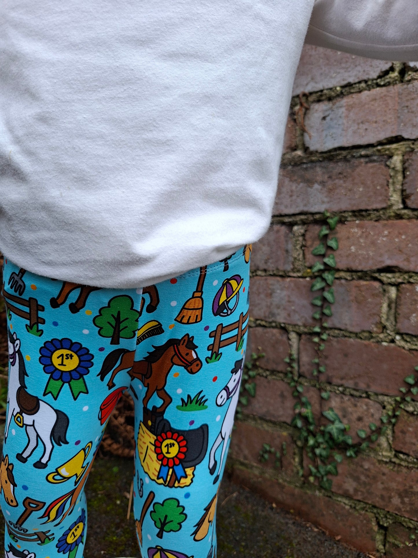 Colorful patterned leggings with horse designs worn by a person against a brick wall.