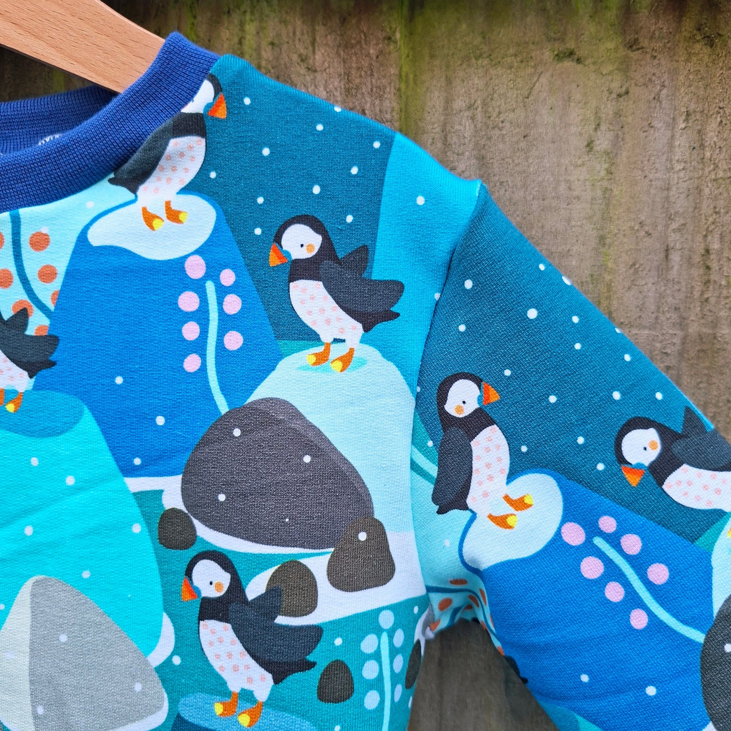 Children's jumper in a puffin print fabric. Pictured against a wooden background 