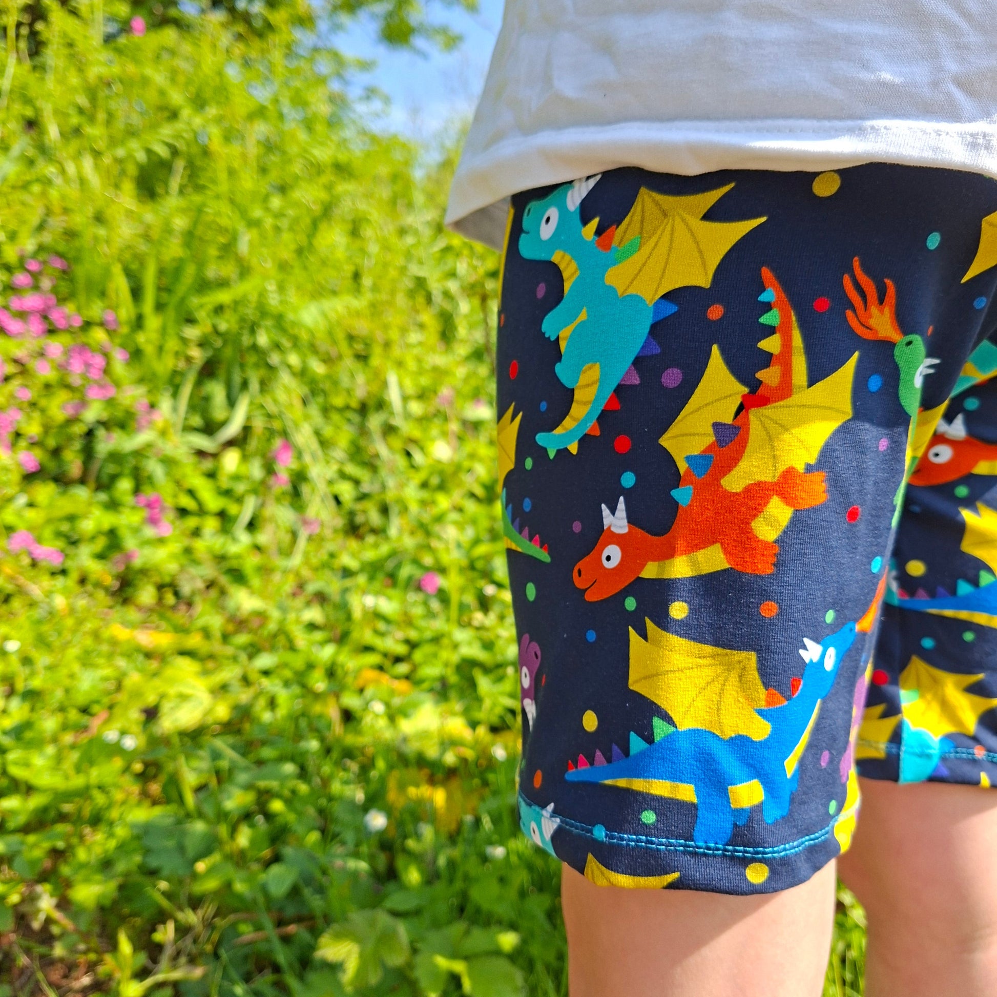 Colourful children's shorts with dragon pattern worn by a person in a grassy outdoor setting