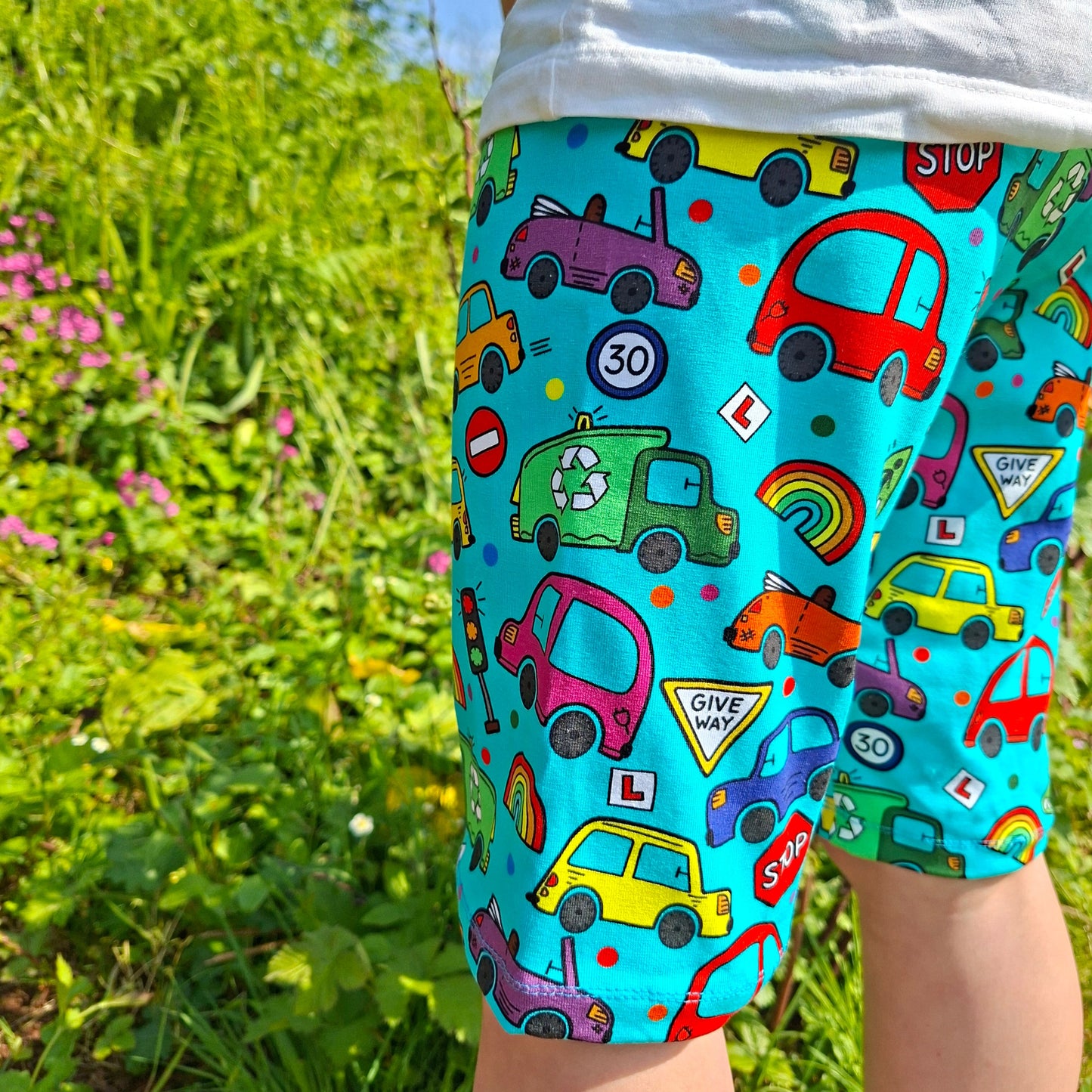 Colourful knee length children's shorts with car pattern worn by a person outdoors.
