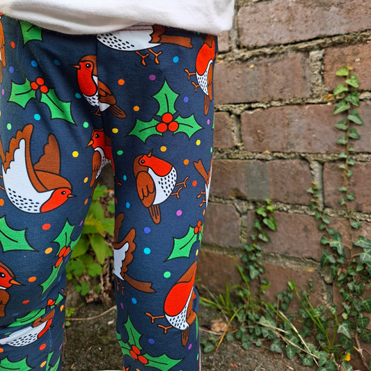 Leggings with Christmas-themed pattern of robins and holly against a brick wall.