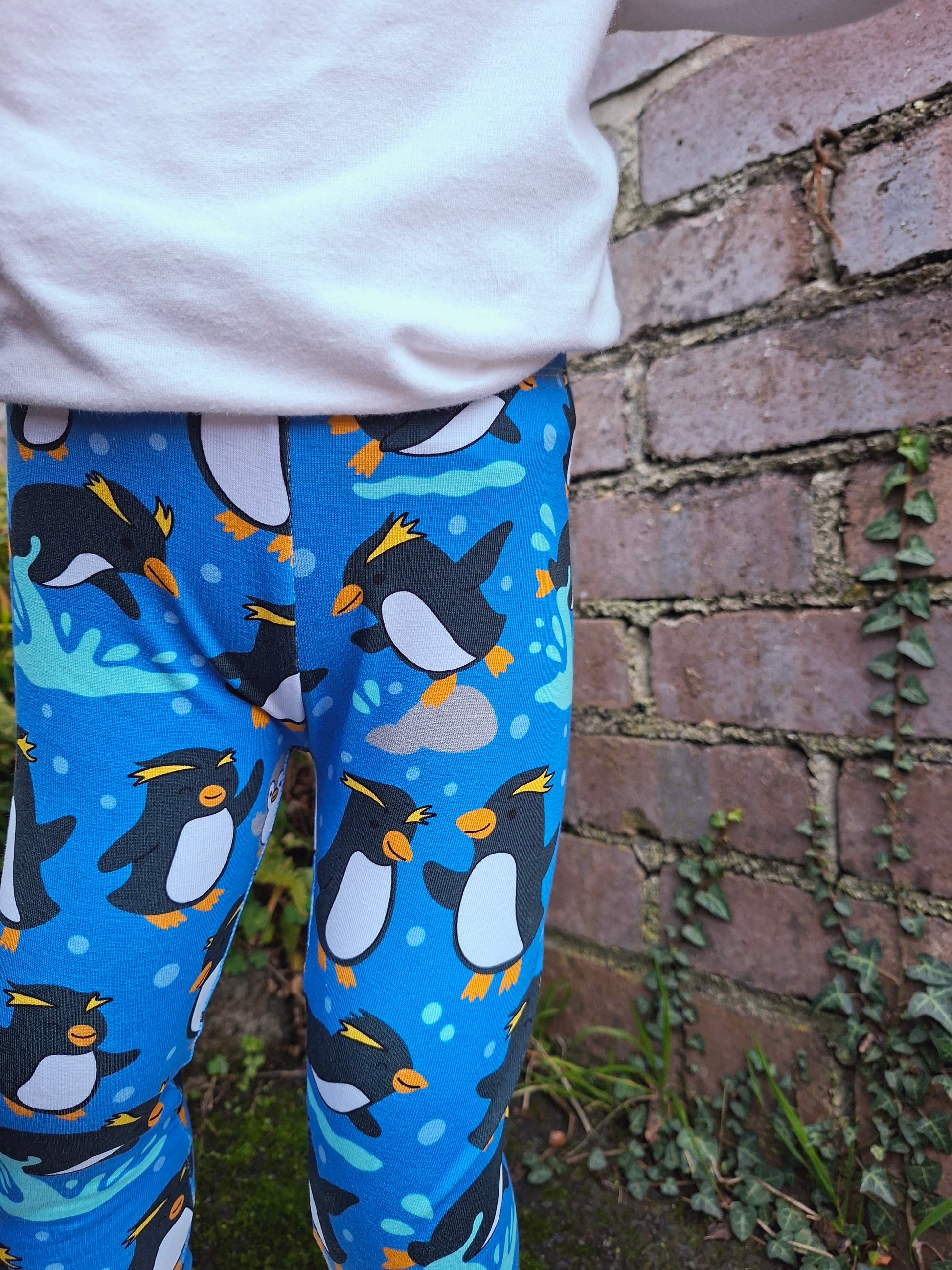 Blue leggings with penguin pattern worn by a child against a brick wall.