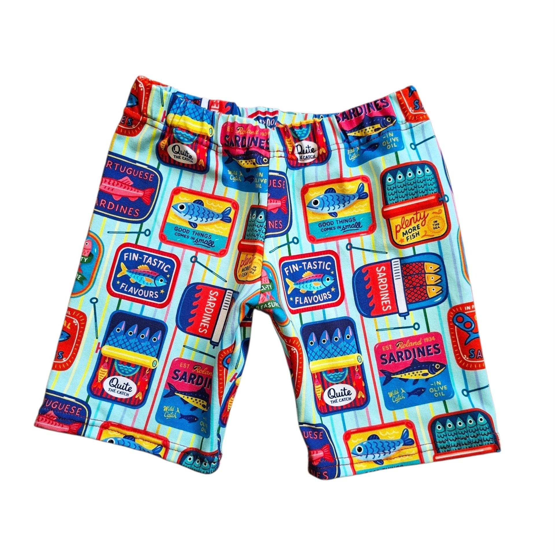 A pair of kids' shorts featuring a colorful cartoon sardine can print on a light blue striped background, displayed flat against a white background.