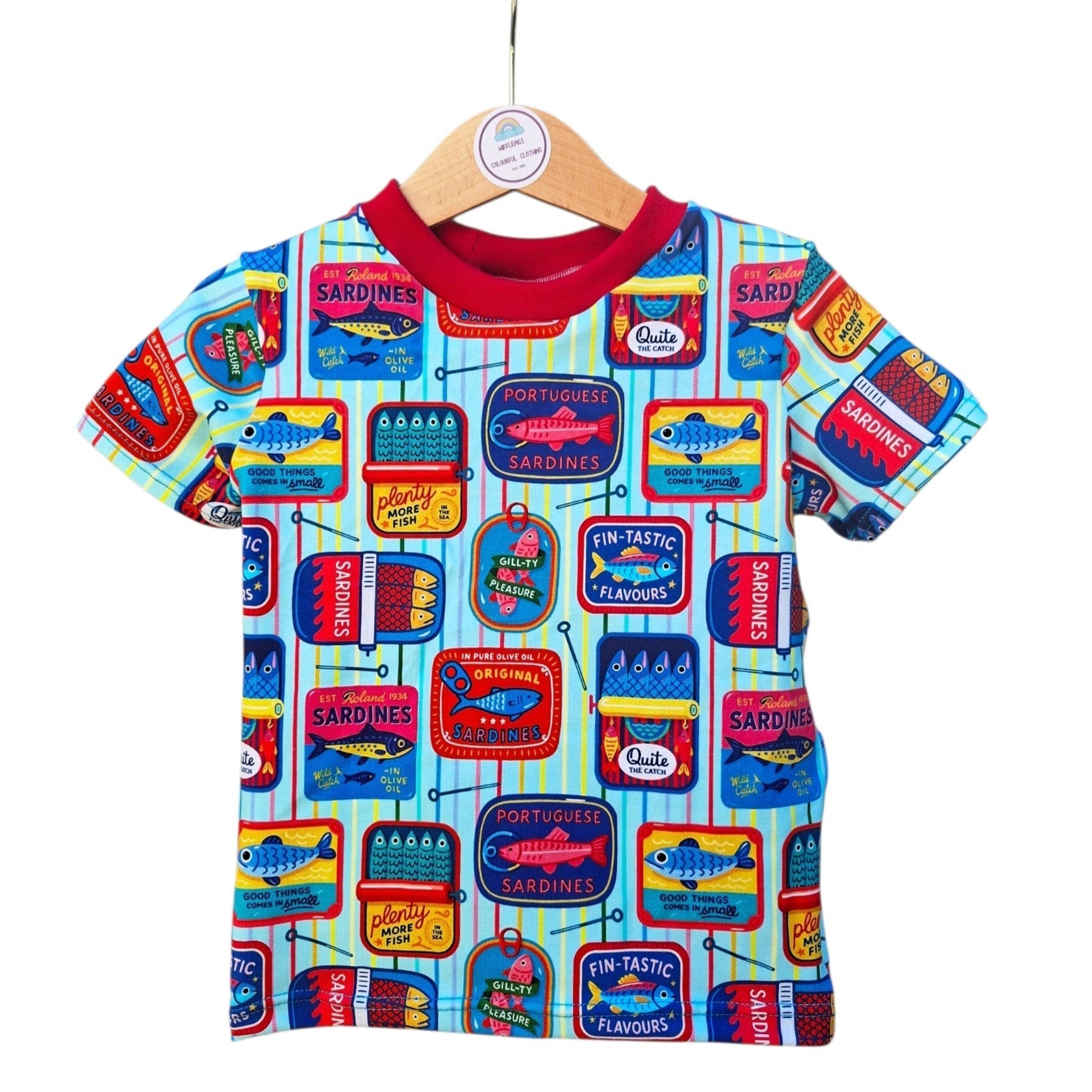 A short-sleeve kids' t-shirt with a colourful sardine tin pattern, hanging on a wooden hanger against a plain white background.