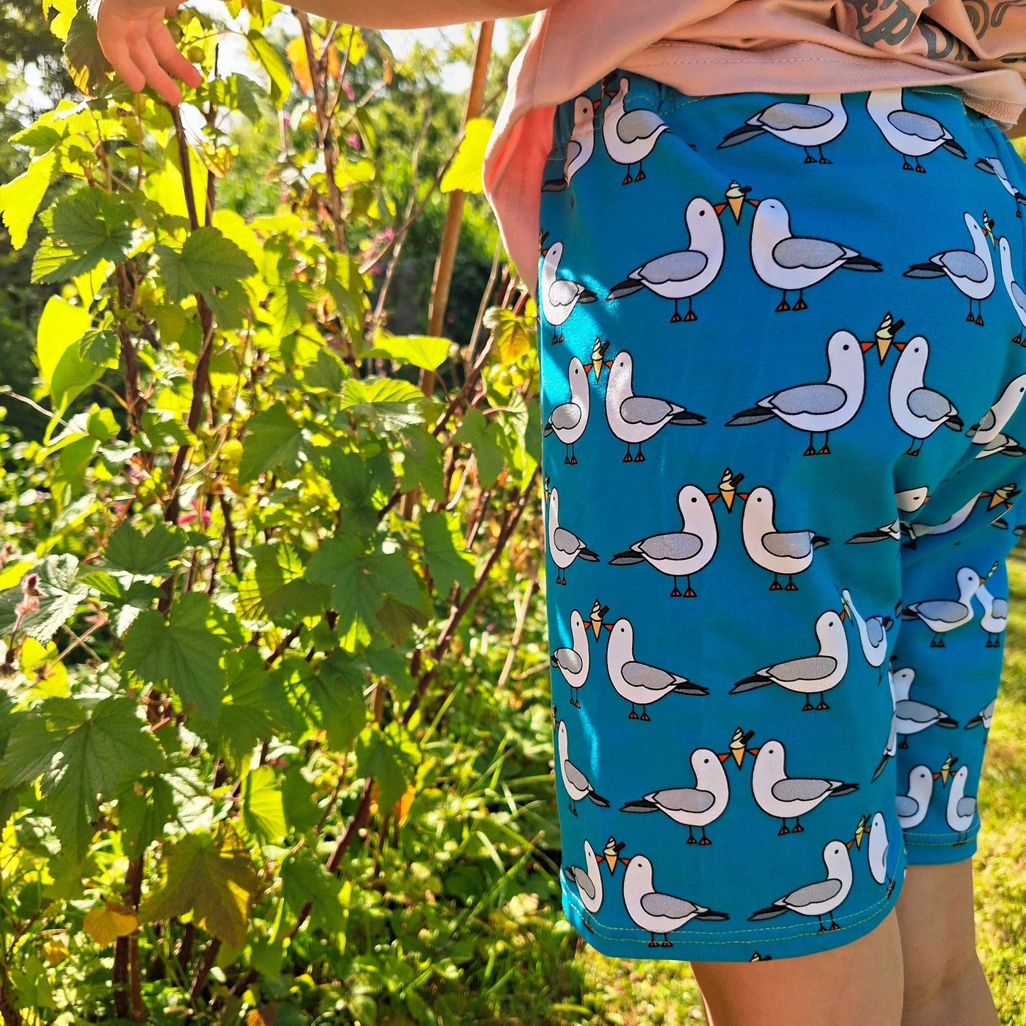 Child wearing blue shorts with seagull pattern in a garden setting
