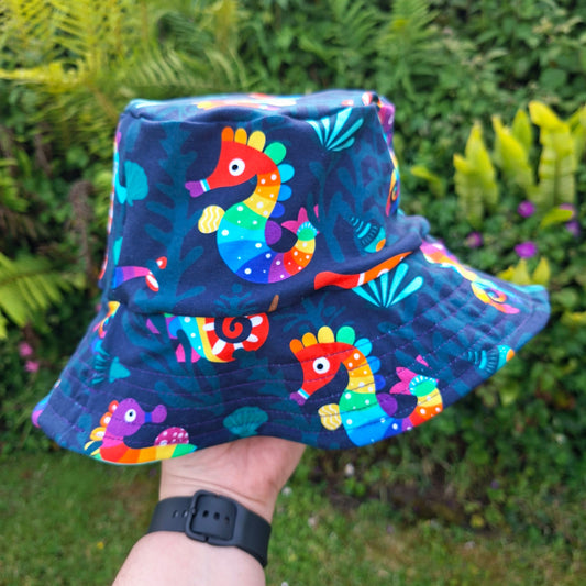 Colourful bucket hat with seahorse design held in front of a green, leafy background