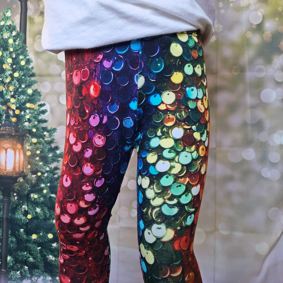 A person wearing colorful sequined leggings with a gradient design, featuring red and blue on one leg and green, yellow, and blue on the other, paired with a white sweatshirt.