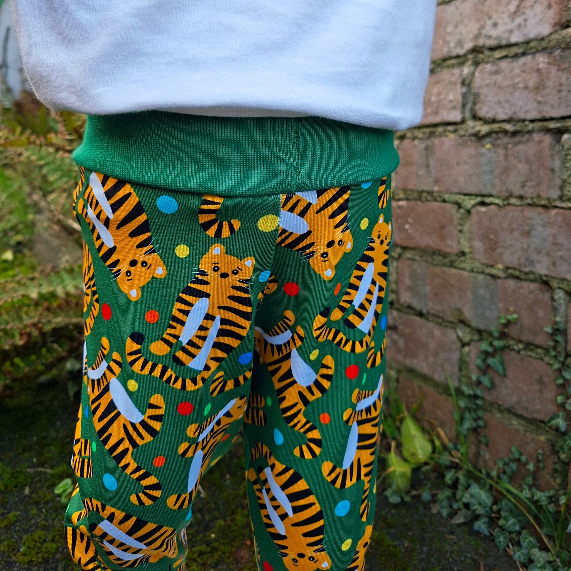 Close-up of a pair of children's trousers green fabric with tiger pattern next to a white fabric
