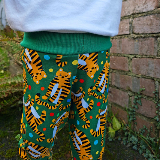 Close-up of a pair of children's trousers green fabric with tiger pattern next to a white fabric