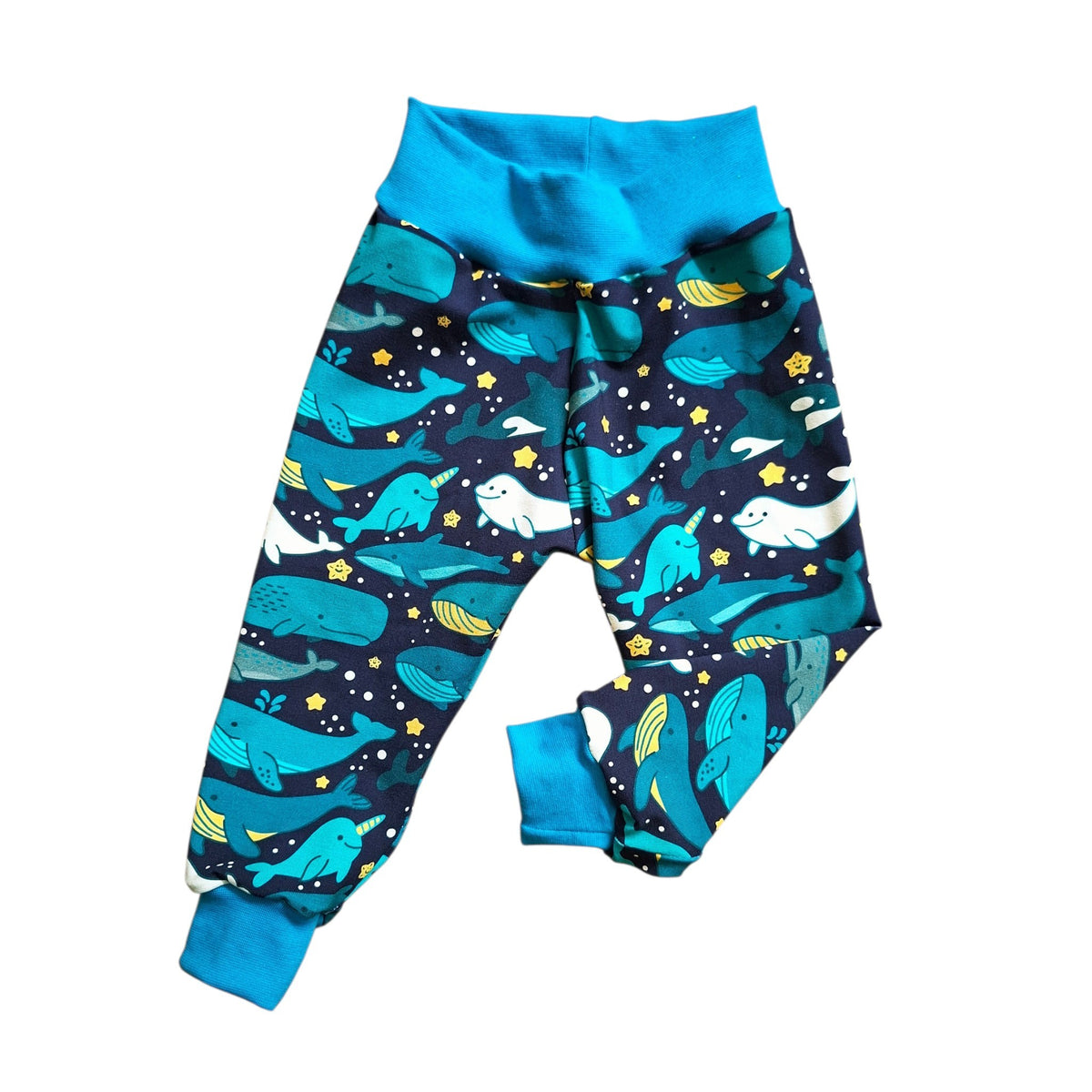 A pair of children's relaxed fit trousers featuring a playful ocean-themed print with blue whales, seals, and yellow stars on a dark navy background, finished with solid bright blue cuffs and waistband.