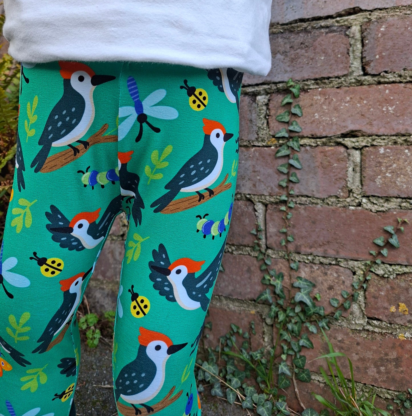 Green leggings with bird and ladybug pattern against a brick wall background