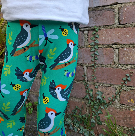 Green leggings with bird and ladybug pattern against a brick wall background