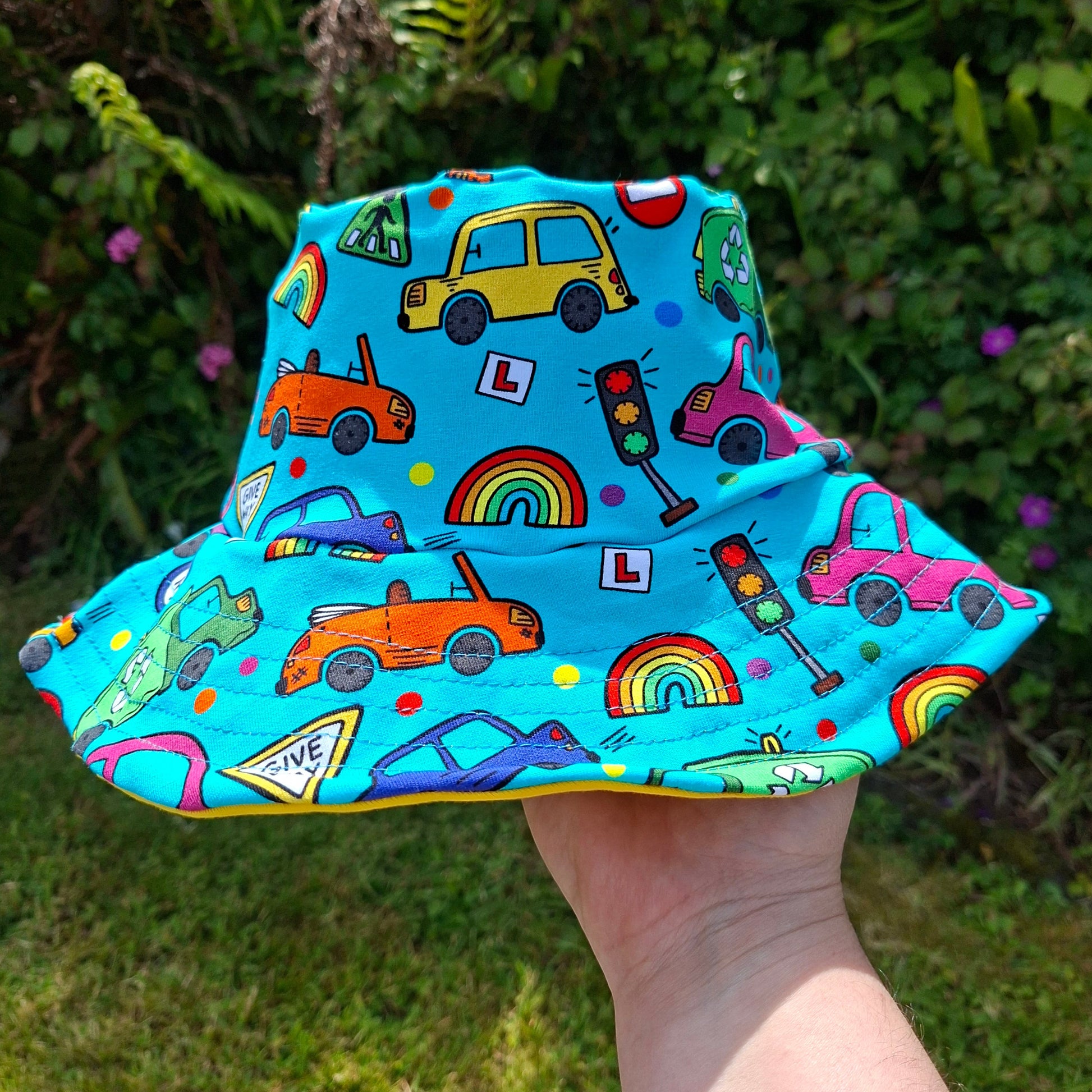 Colorful children's bucket hat with car pattern held by a hand against a green outdoor background