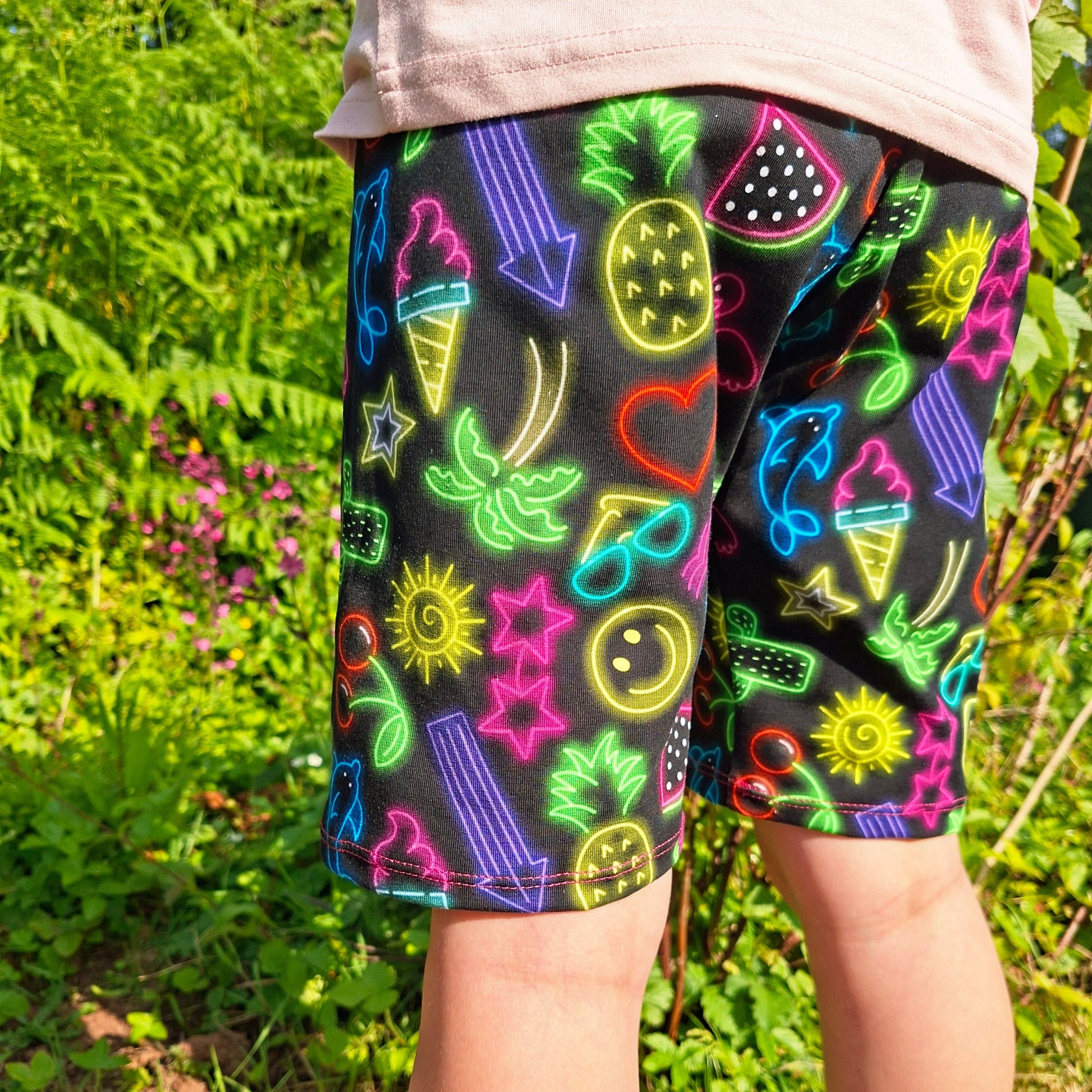 Colourful children's shorts in a black fabric with neon designs worn by a child outdoors.
