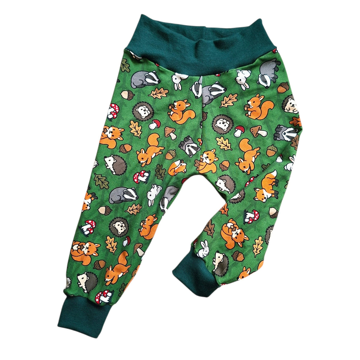 Green children's relaxed fit trousers with a woodland animal print featuring foxes, hedgehogs, rabbits, and acorns, finished with dark green ribbed cuffs and waistband.