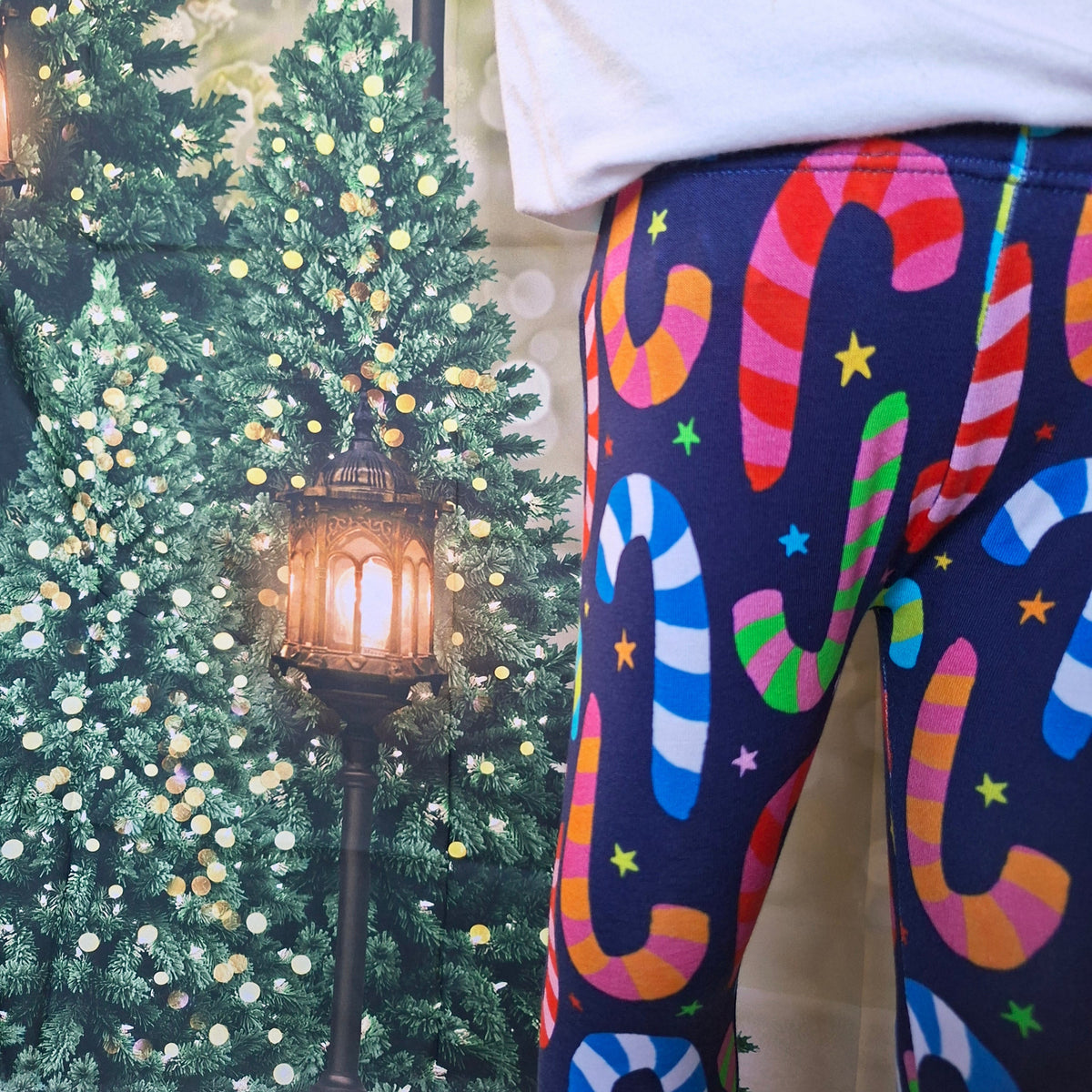 Candy cane print leggings worn with a white top beside Christmas trees